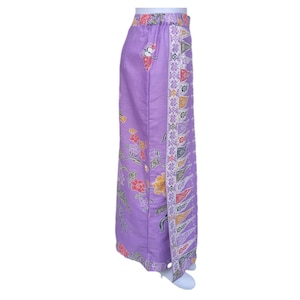 May include: A lavender-colored skirt with a floral and geometric pattern. The skirt features a side slit and a decorative border with red, yellow, and green accents. The floral design includes red, yellow, and pink flowers with green leaves.