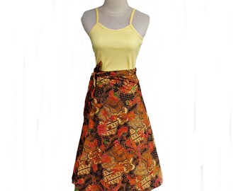 May include: A brown and orange patterned wrap skirt with a yellow tank top on a mannequin. The skirt has a floral design and is tied at the waist.