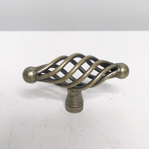 Peut inclure: Un bouton de porte décoratif avec un design torsadé en forme de cage, finition laiton antique.