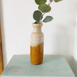 Peut inclure: Un vase en céramique avec un glaçage blanc et brun, présentant un motif marbré. Le vase est rempli d'une branche d'eucalyptus.