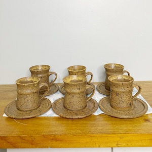 Peut inclure: Ensemble de six tasses à café et soucoupes en céramique mouchetée de brun. Les tasses et les soucoupes ont un aspect rustique et artisanal.