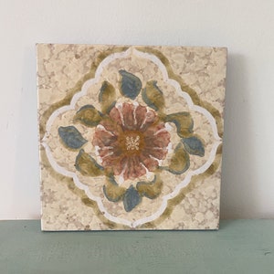 Peut inclure: Un carreau de céramique carré avec un motif floral. Le carreau est beige avec une bordure blanche et un motif floral brun, rose et bleu au centre.