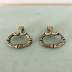 Puede incluir: Dos tiradores de armario de latón antiguo con un diseño decorativo. Los tiradores son de forma ovalada con un borde elevado y un diseño decorativo en la parte superior e inferior.