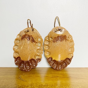 May include: Two brown ceramic wall pockets with a textured surface and a hanging loop. Each pocket has a scalloped edge and a raised design of small circles.