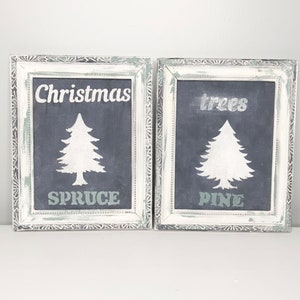 Op de afbeelding: Twee witte geframed krijtborden met een verweerde afwerking. De borden tonen witte silhouetten van kerstbomen met de woorden "Christmas Spruce" en "trees Pine" in wit.