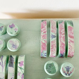 Peut inclure: Une collection de poignées et de boutons de tiroir décoratifs avec des motifs floraux et de papillons. Les poignées et les boutons sont peints en vert clair et présentent une variété de motifs floraux, notamment des roses, des papillons et des feuilles.