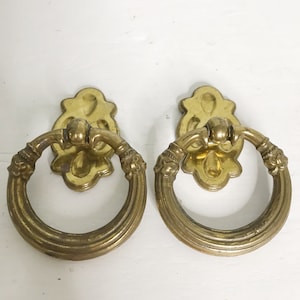 Peut inclure: Deux poignées de tiroir en métal doré avec une poignée en anneau et un motif floral orné.