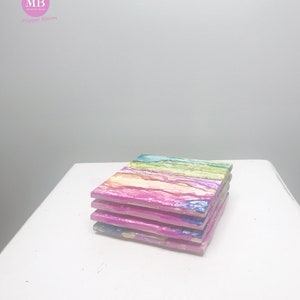 May include: Set of four colorful coasters with abstract, swirled patterns in shades of pink, blue, green, and yellow. The coasters are stacked on top of each other.