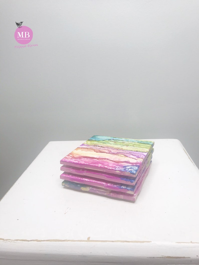 May include: Set of four colorful coasters with abstract, swirled patterns in shades of pink, blue, green, and yellow. The coasters are stacked on top of each other.