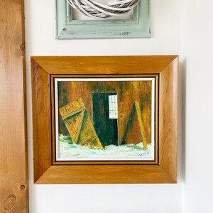 Peut inclure: Une peinture encadrée représentant une grange avec une porte en bois et une fenêtre. La grange est peinte dans des tons de brun, jaune et vert. La peinture est sur un fond blanc.