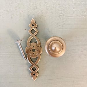 Peut inclure: Un ensemble de deux boutons de cabinet argentés avec un design orné. Un bouton est rond et l'autre est un long rectangle mince avec un motif décoratif.