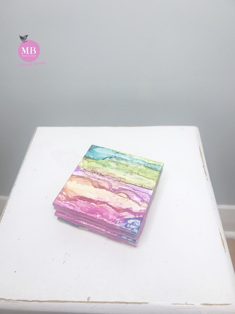 May include: A set of four colorful coasters with abstract patterns in shades of pink, blue, green, and yellow. The coasters are made of a smooth, absorbent material and are perfect for protecting surfaces from spills and heat.