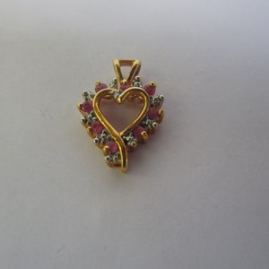 May include: A gold heart-shaped pendant with a delicate openwork design. The pendant is adorned with small pink and white gemstones.