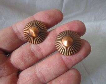 May include: A pair of copper earrings with a sunburst design. The earrings are round and have a raised center.