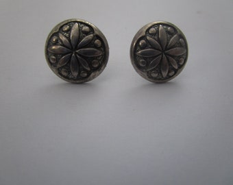 May include: A pair of silver earrings with a floral design. The earrings are round and have a textured surface.