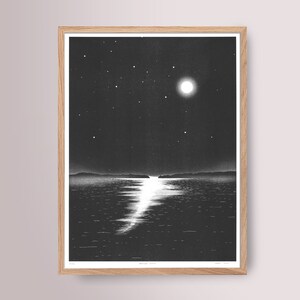 May include: Monochrome print of a moonlit seascape, framed in natural wood. The artwork shows a bright full moon and stars above calm water, with the moon's reflection creating a shimmering path. The print is signed and numbered.