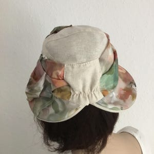 May include: A beige and floral print hat with a brim. The hat features a beige crown and a brim with a colorful floral pattern in shades of pink, green, and orange. The hat is designed for sun protection.