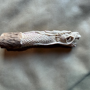 May include: A carved handle featuring a detailed dragon head with visible scales and an open mouth, transitioning into a rough, textured brown base. The dragon portion is light beige, showcasing intricate craftsmanship and defined facial features.
