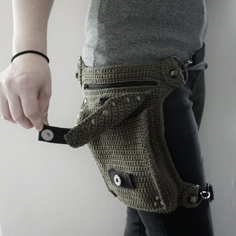 May include: A green crocheted fanny pack with a black strap and silver studs. The pack has a zippered pocket and a flap with a snap closure.