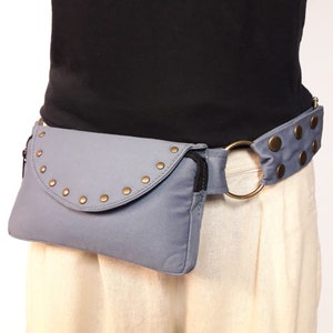 May include: A gray canvas fanny pack with a zipper closure and a metal ring. The fanny pack has a flap with a half-circle design and is adorned with silver studs. The fanny pack is worn around the waist with a matching gray canvas belt.