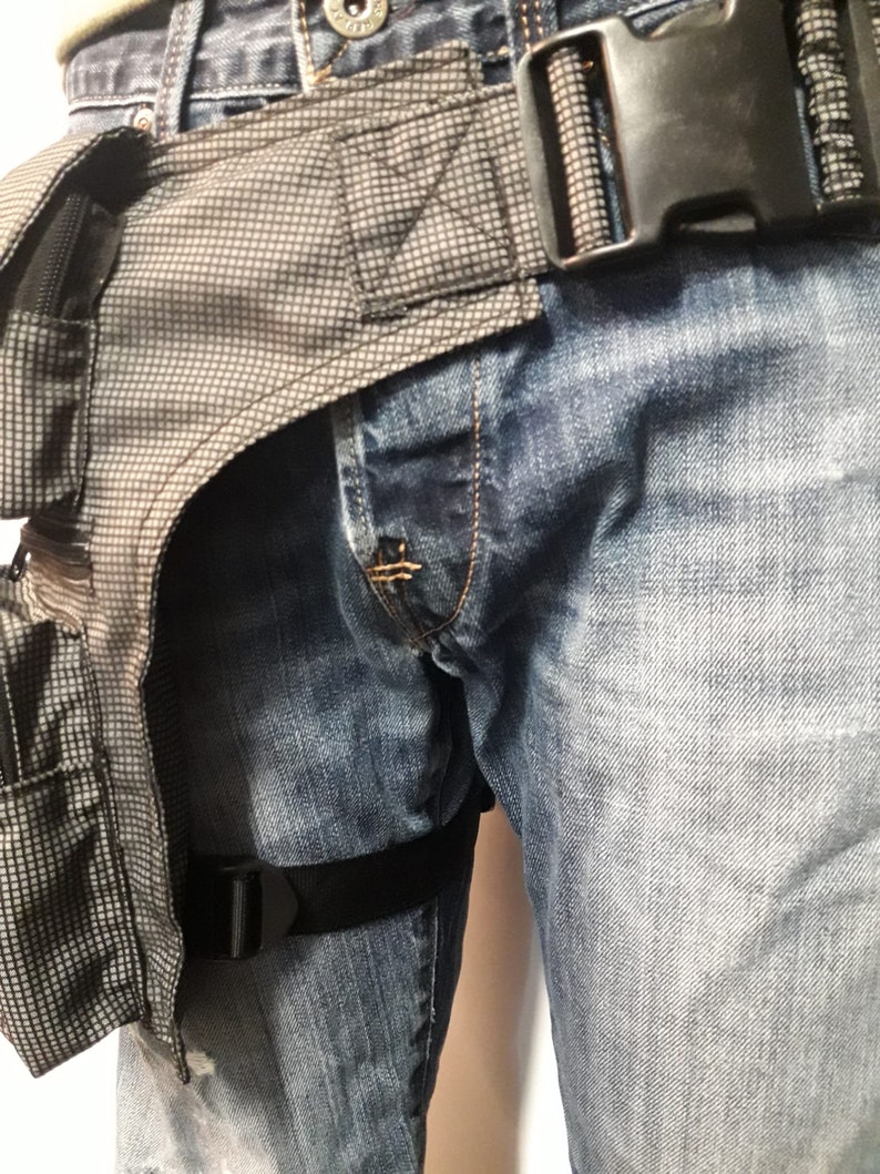 Puede incluir: Una correa de pierna t&aacute;ctica negra con una bolsa t&aacute;ctica gris y negra unida a ella. La correa se lleva sobre un par de pantalones vaqueros azules.