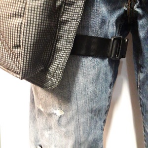 Puede incluir: Un par de pantalones vaqueros azules con una correa negra y una bolsa de patr&oacute;n gris y negro unida a la correa.