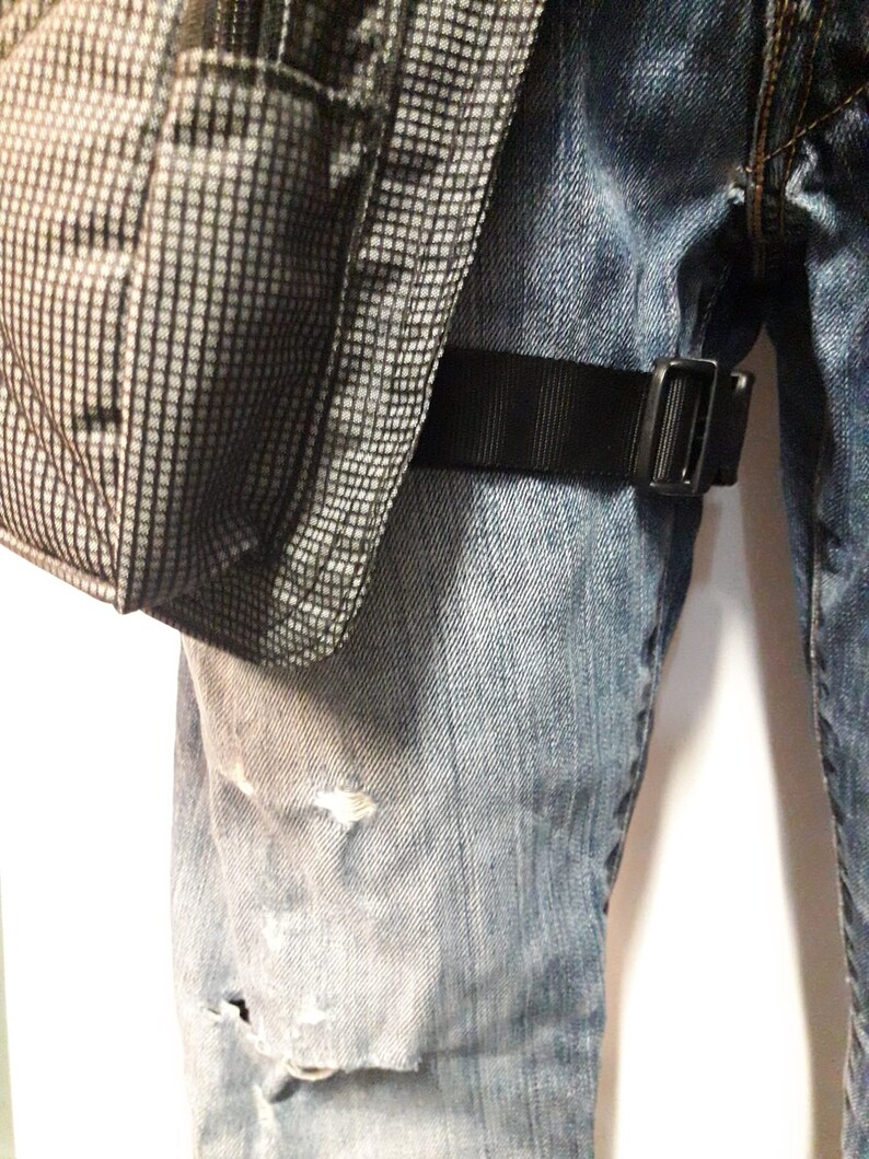 Puede incluir: Un par de pantalones vaqueros azules con una correa negra y una bolsa de patr&oacute;n gris y negro unida a la correa.