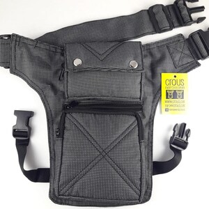 Puede incluir: Una bolsa de muslo a cuadros en negro y gris con m&uacute;ltiples bolsillos y correas ajustables. La bolsa tiene un bolsillo con cremallera en la parte delantera y un bolsillo con cremallera m&aacute;s peque&ntilde;o en el lateral. La bolsa tiene una hebilla negra en la correa. La bolsa tiene una etiqueta amarilla con el texto "Crous Eat Color Live" y una direcci&oacute;n de sitio web.