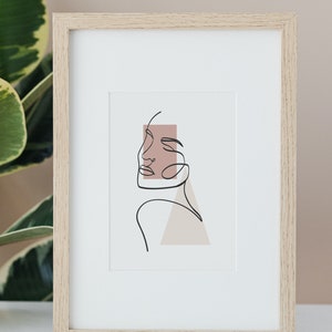 May include: A framed print of a line drawing of a face with a pink and beige background.