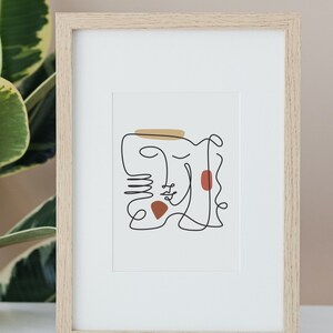 May include: A framed abstract line drawing of two faces with brown and gold accents. The drawing is on a white background and is framed in a light wood frame.
