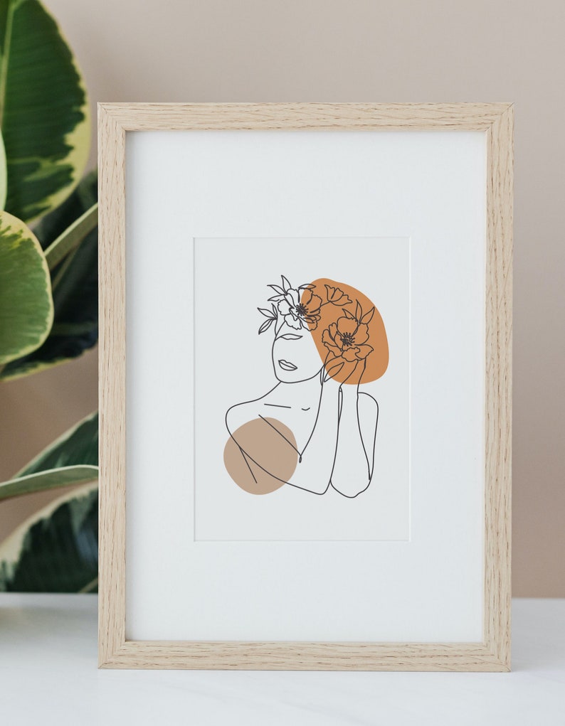 May include: A framed print of a line drawing of a person with flowers in their hair. The drawing is in black and white, and the background is a light brown color.