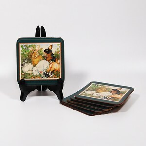 May include: Set of four green and brown square coasters with a colorful illustration of rabbits. The coasters are stacked on top of each other.