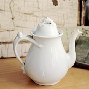 May include: White porcelain teapot with a lid and a decorative handle. The teapot has a classic design and is perfect for serving tea.