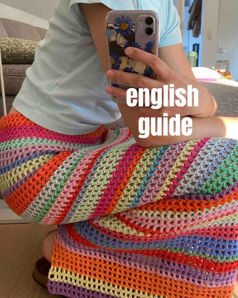 May include: A person wearing a light blue shirt and a colorful crochet skirt. The skirt is made of a variety of colors, including pink, orange, yellow, green, and blue. The skirt is crocheted in a pattern of stripes and squares. The person is holding a cell phone with a floral case. The text "english guide" is written on the image.