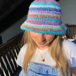 May include: A colorful crocheted bucket hat with stripes of pink, blue, green, and purple.