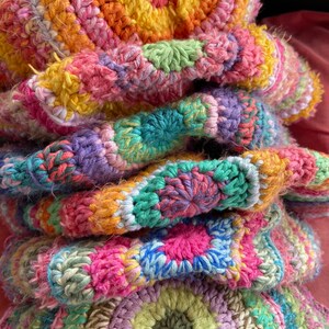 May include: A stack of colorful crocheted blankets in shades of pink, green, yellow, and purple. The blankets are made with a variety of stitches and textures, creating a unique and eye-catching design.