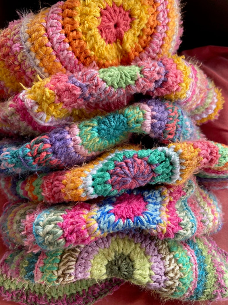 May include: A stack of colorful crocheted blankets in shades of pink, green, yellow, and purple. The blankets are made with a variety of stitches and textures, creating a unique and eye-catching design.
