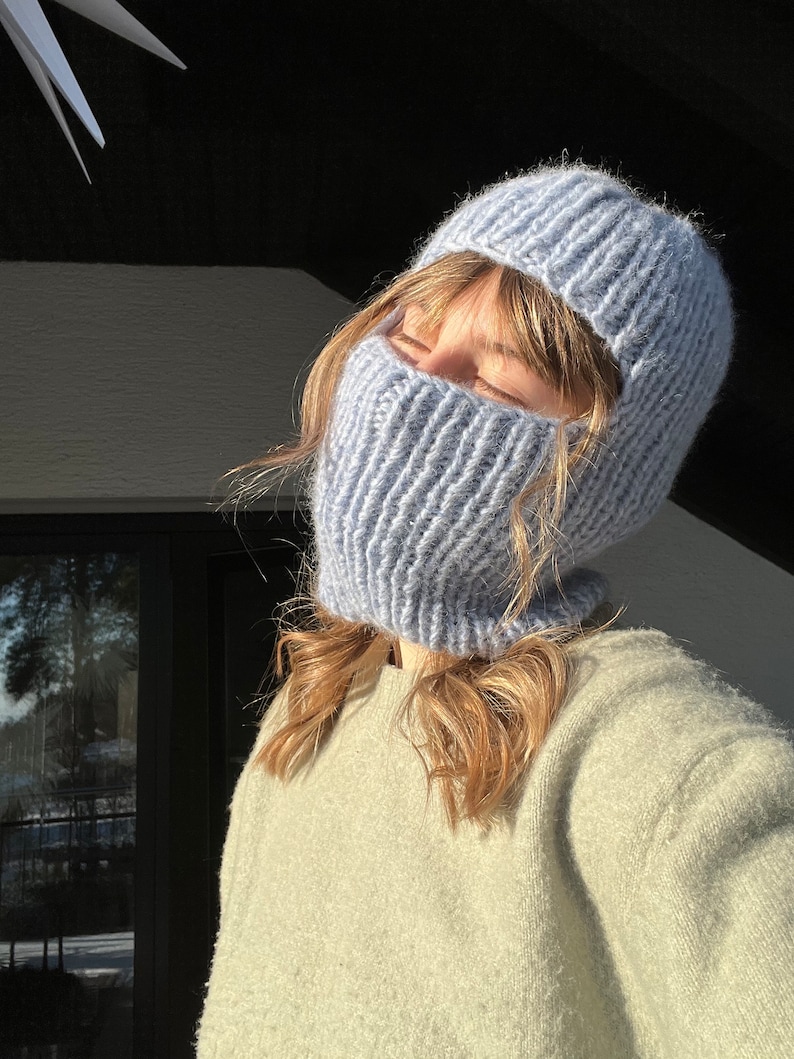 May include: A light blue knitted balaclava with a hole for the eyes and mouth. The balaclava is made of a soft, fuzzy yarn.