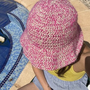 May include: A pink and white crocheted bucket hat with a wide brim.