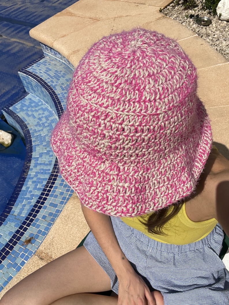 May include: A pink and white crocheted bucket hat with a wide brim.