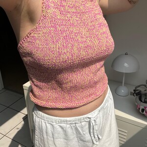 May include: A pink and yellow knit halter top. The top is a sleeveless design with a ribbed hem and neckline. The knit fabric has a speckled appearance. The top is paired with white drawstring pants.