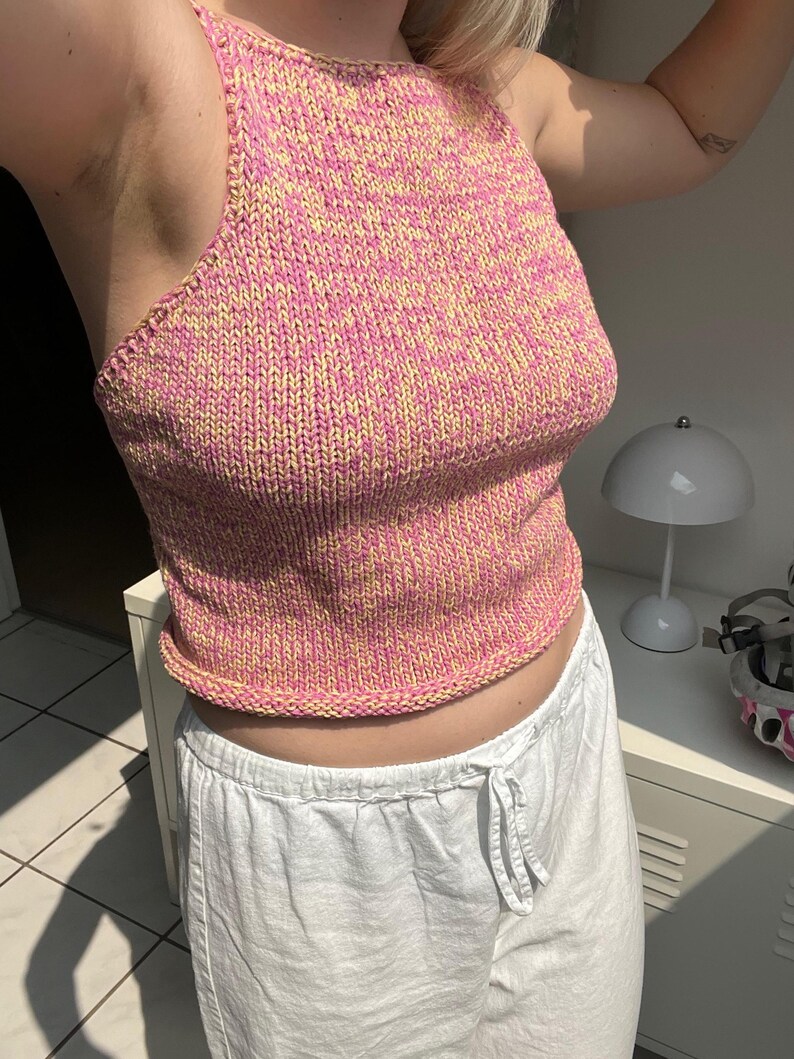 May include: A pink and yellow knit halter top. The top is a sleeveless design with a ribbed hem and neckline. The knit fabric has a speckled appearance. The top is paired with white drawstring pants.