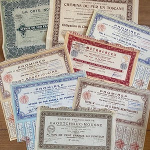 May include: A selection of antique French stock certificates, with elaborate borders and French text. The certificates are in shades of blue, red, and beige, arranged on a wooden surface. The certificates are from various companies, and are of historical interest.