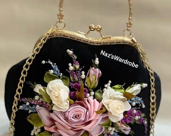 May include: Black handbag with a gold chain strap and handle. The bag features a floral design with pink, white, and purple roses, along with pearls and green leaves. The text "Naz'sWardrobe" is visible on the bag.