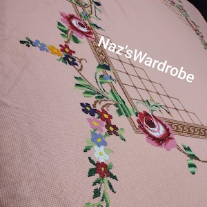 May include: A pink tablecloth with embroidered floral designs. The embroidery features red, pink, and white roses, along with other colorful flowers and green leaves. The text "Naz's Wardrobe" is visible.