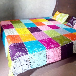 May include: A colorful crocheted bedspread with a patchwork design in shades of pink, purple, blue, green, orange, and yellow. The bedspread is made of squares with a lacy pattern.
