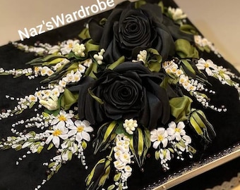 May include: A black decorative box adorned with large black silk roses, white flowers, and green leaves. The box is embellished with delicate white accents and the text "Naz's Wardrobe".