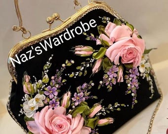May include: A black velvet handbag with a gold clasp and chain strap. The bag is decorated with pink and purple ribbon flowers.