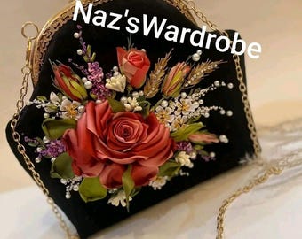 May include: Black handbag with a gold chain strap and clasp. The bag is decorated with a large red rose and other floral accents. The text "Naz'sWardrobe" is printed on the bag.
