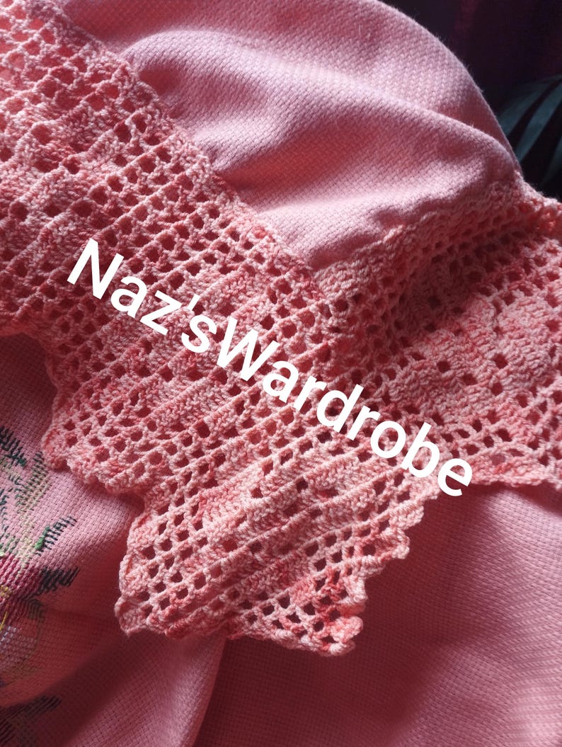May include: Close-up of a pink garment with a crocheted lace trim. The lace is a lighter shade of pink and features a delicate openwork design. The text "Naz's Wardrobe" is visible on the garment.
